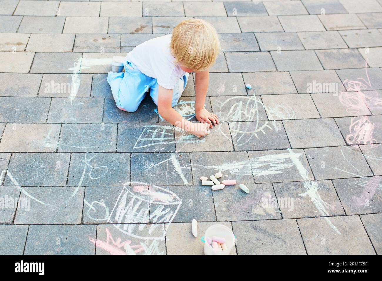 Adorable little boy drawing with colorful chalks on asphalt. Summer ...