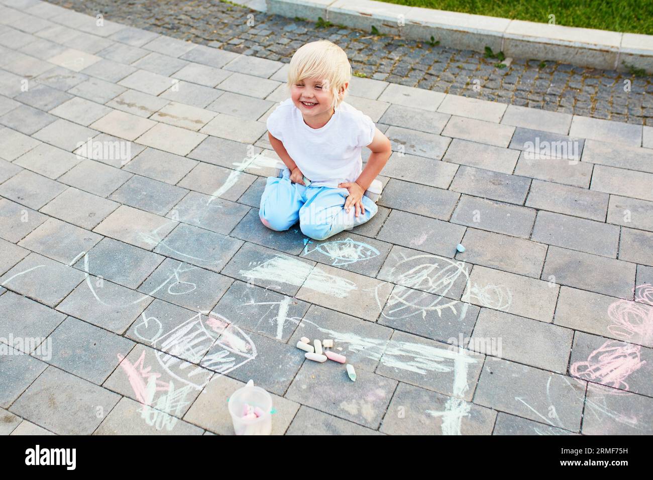 Adorable little boy drawing with colorful chalks on asphalt. Summer ...
