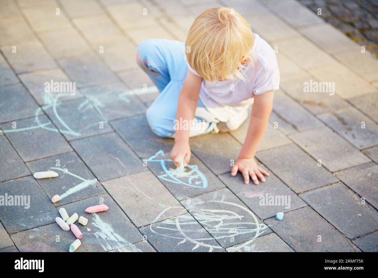 Adorable little boy drawing with colorful chalks on asphalt. Summer ...