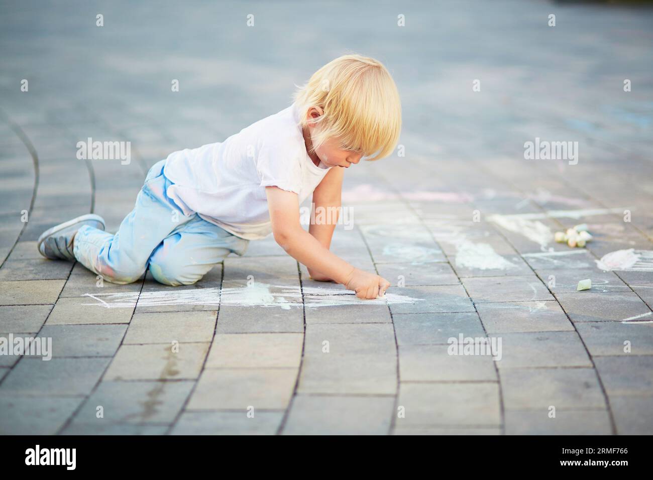 Adorable little boy drawing with colorful chalks on asphalt. Summer ...