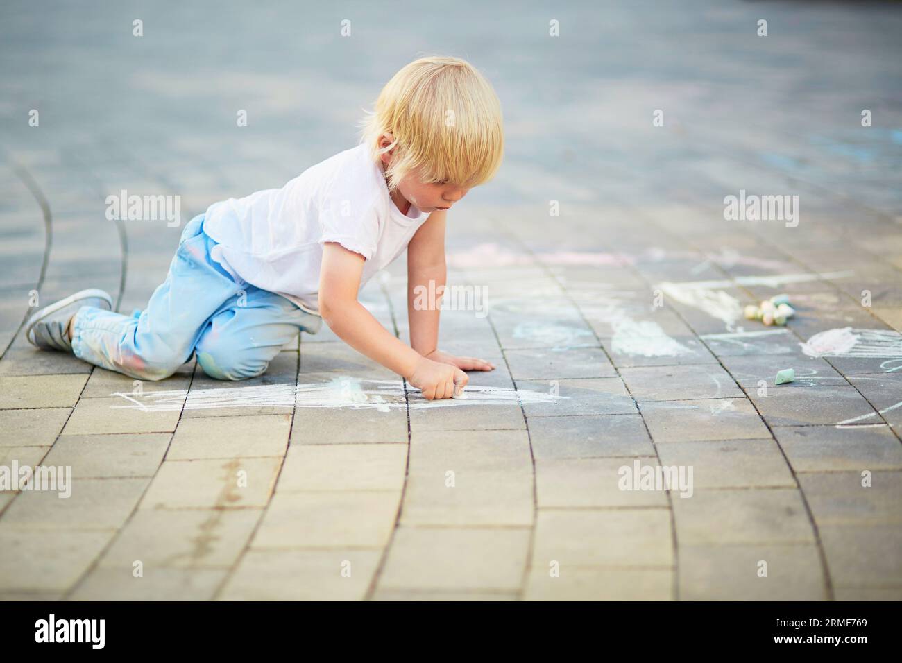 Adorable little boy drawing with colorful chalks on asphalt. Summer ...