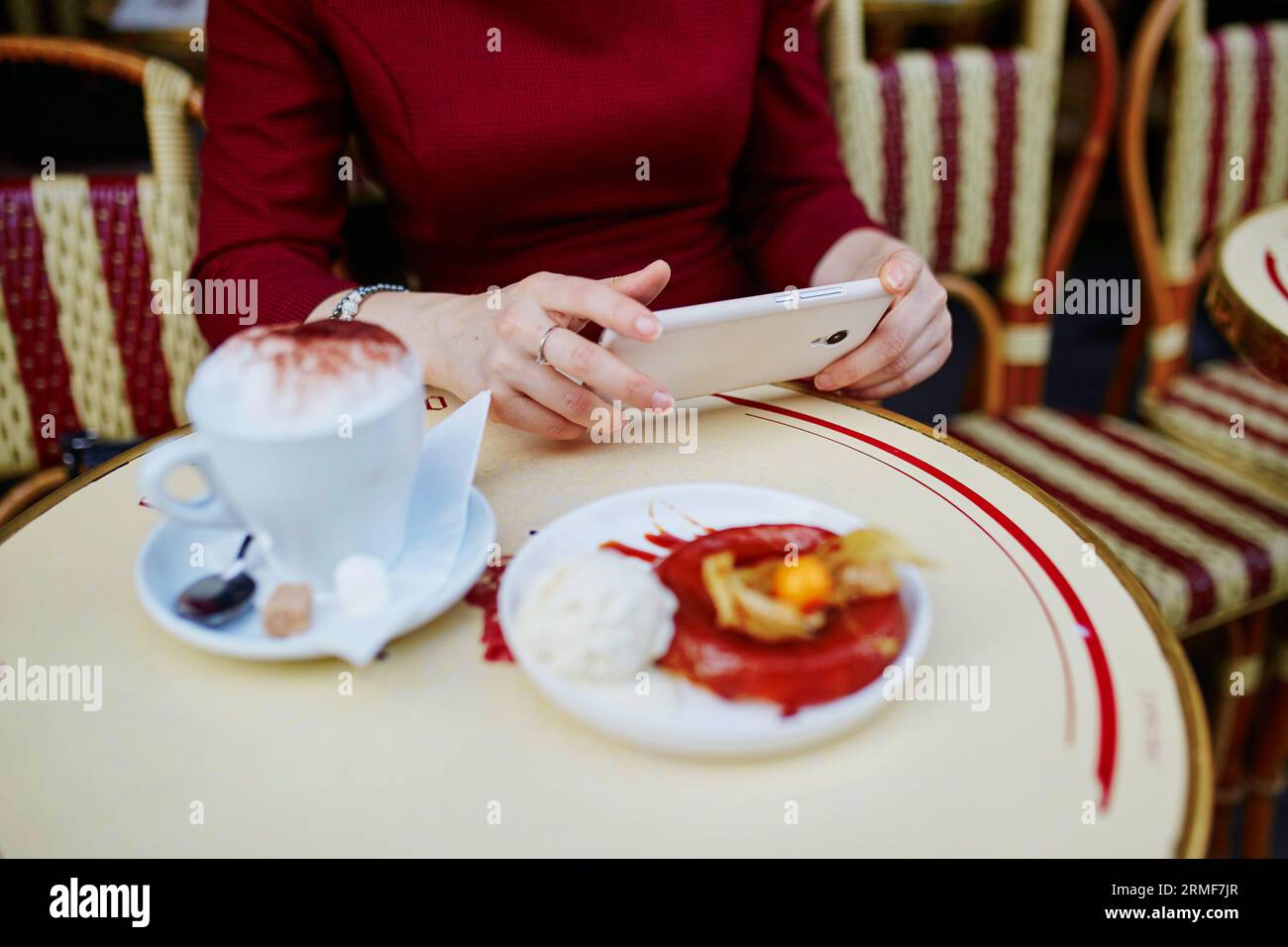 French woman drinking coffee in outdoor cafe in Paris, France and using her mobile phone for texting, browsing or photo. Closeup of hands holding gadg Stock Photo