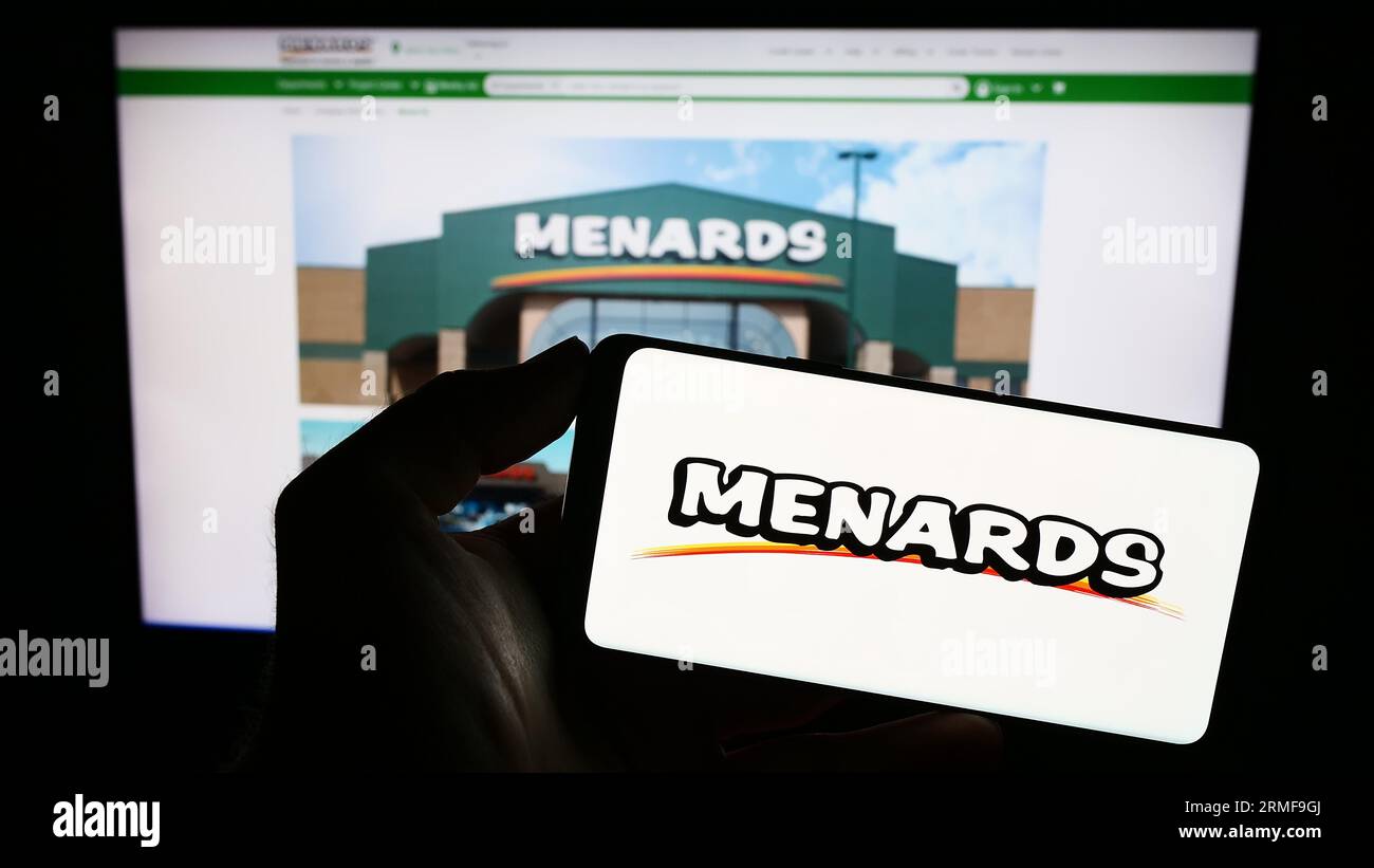 Person holding smartphone with logo of US retail company Menard Inc. (Menards) on screen in front of website. Focus on phone display. Stock Photo