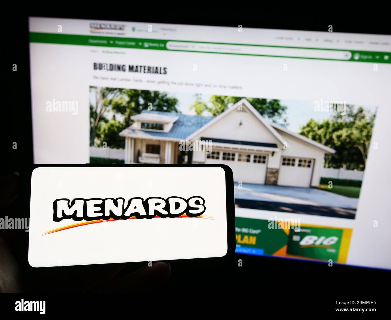 Person holding mobile phone with logo of American retail company Menard Inc. (Menards) on screen in front of web page. Focus on phone display. Stock Photo