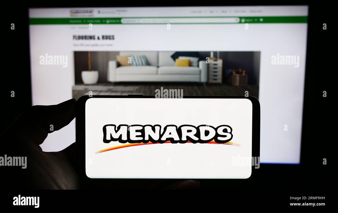 Person holding cellphone with logo of US retail company Menard Inc. (Menards) on screen in front of business webpage. Focus on phone display. Stock Photo
