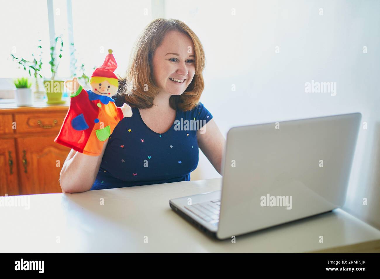 Kindergarten teacher in front of laptop having video conference chat with children. Woman entertaining little kids remotely. Online remote learning an Stock Photo
