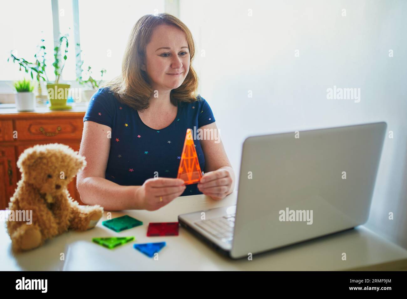 Kindergarten teacher in front of laptop having video conference chat with children. Woman entertaining little kids remotely. Online remote learning an Stock Photo