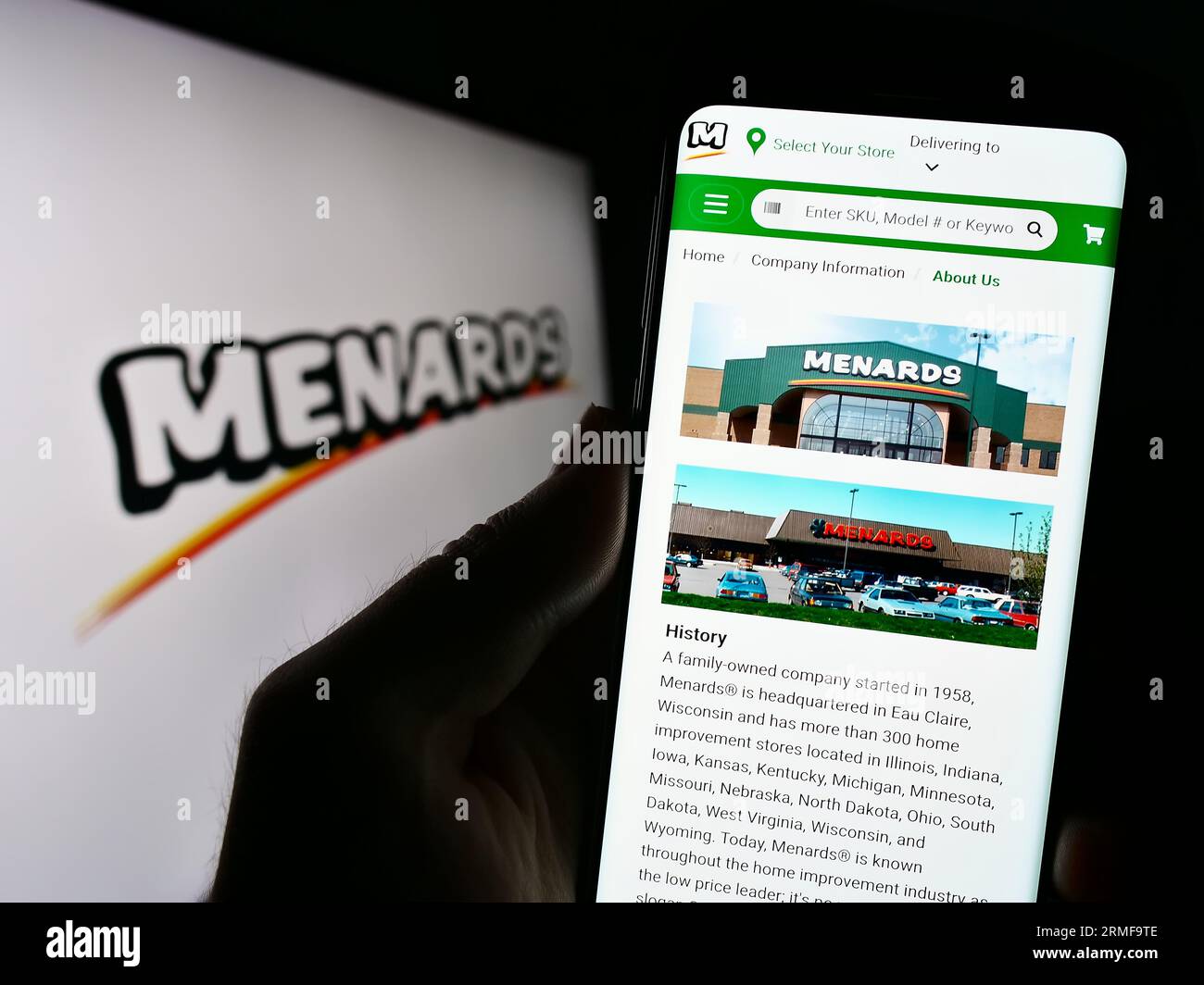 Person holding cellphone with website of US retail company Menard Inc. (Menards) on screen in front of logo. Focus on center of phone display. Stock Photo