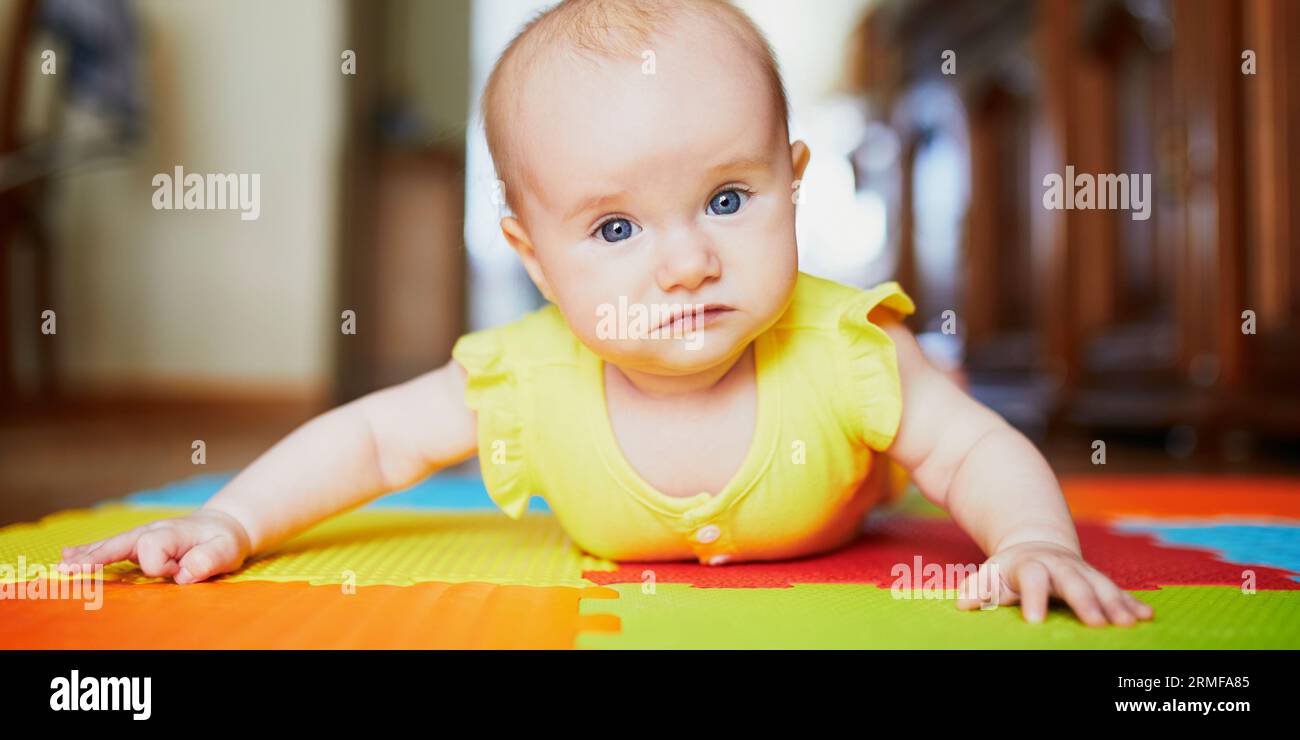 Adorable baby girl doing tummy time on colorful play mat Stock Photo