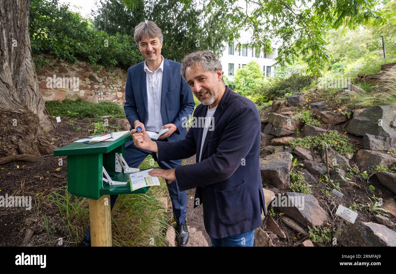 28 August 2023, Saxony-Anhalt, Halle (Saale): Matthias Lux (l), Managing Director of Stadtwerke Halle, and Andreas Nowak, Managing Director of Mitteldeutsches Multimediazentrum, open the new Harzer Wandernadel stamp station in the Botanical Garden in Halle/Saale. Both are passionate hikers and in possession of a hiking pass. Hikers will find a total of over 400 stamping stations in Saxony-Anhalt, Lower Saxony and Thuringia. The stamps are pressed into a previously purchased hiking passport. 222 stamp impressions are necessary to become the 'Harzer Wanderkaiser' or 'Wanderkaiserin'. Photo: Hend Stock Photo