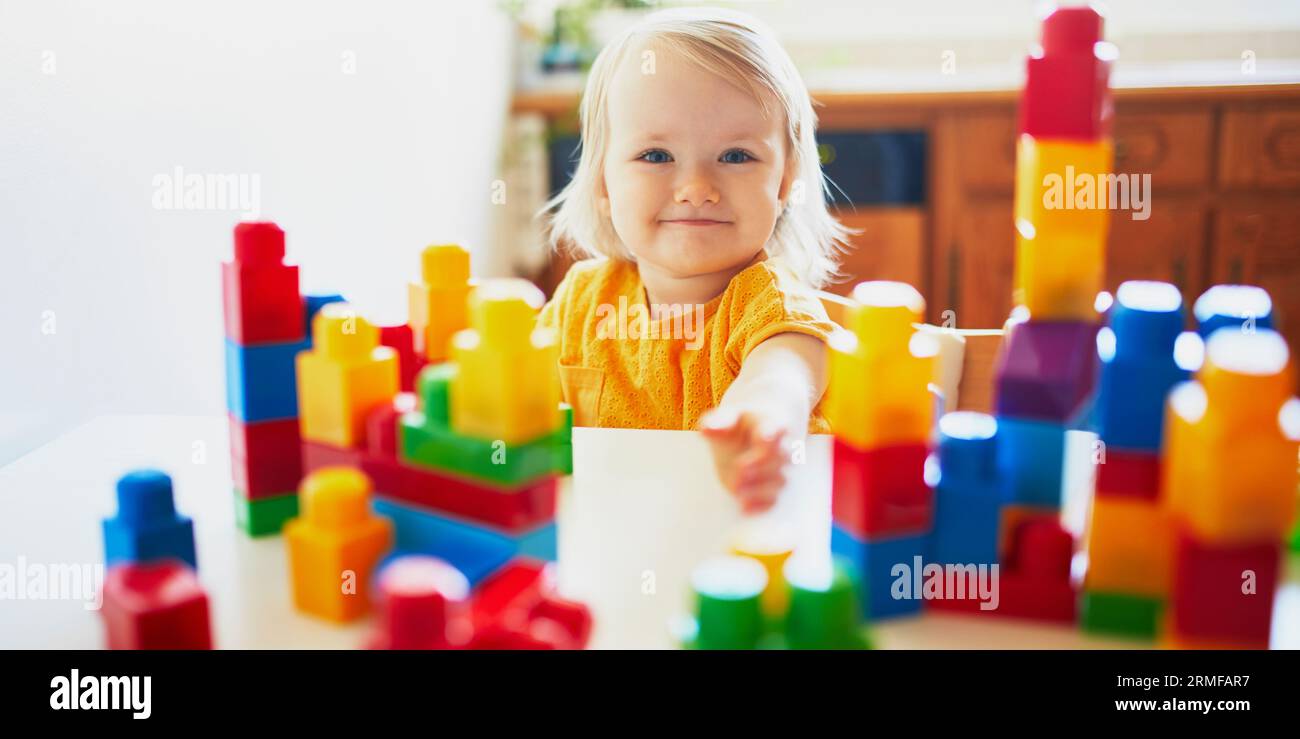 Adorable little girl playing with colorful plastic construction blocks ...
