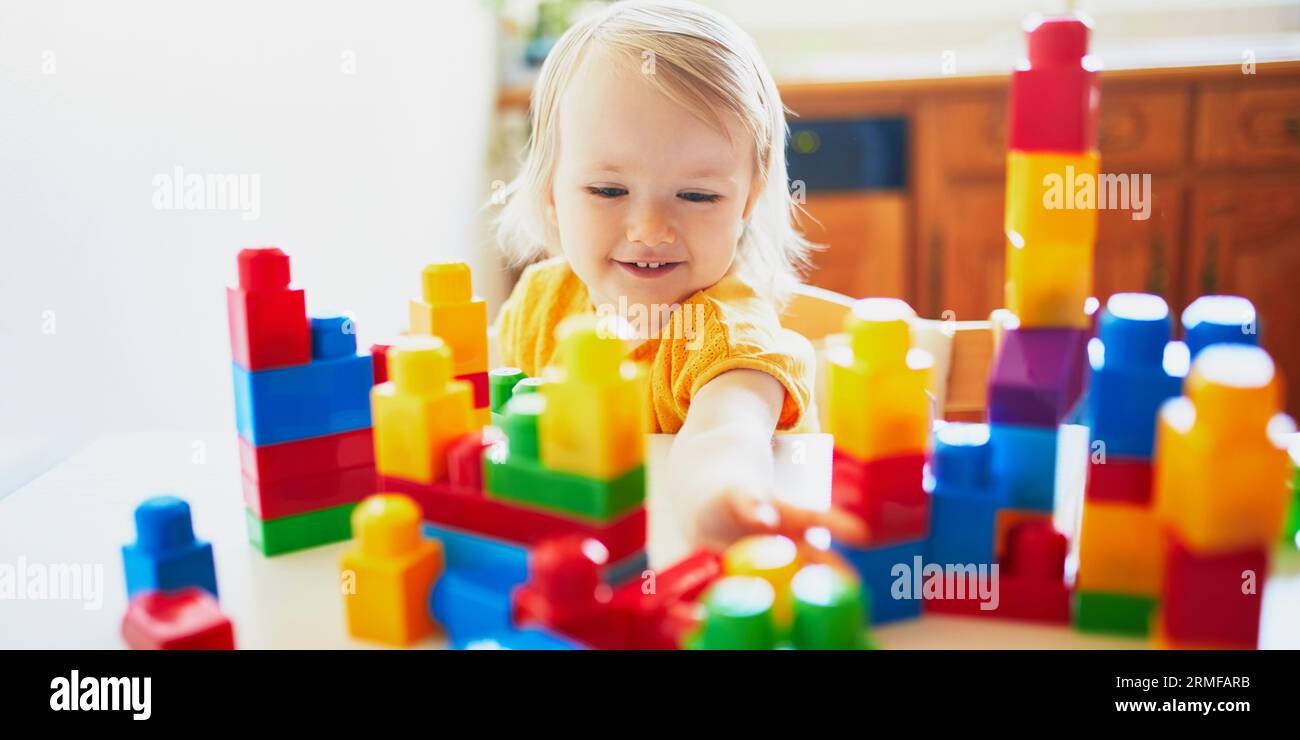 Adorable little girl playing with colorful plastic construction blocks ...