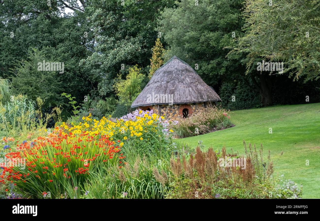 Bressingham, Norfolk, UK – August 21 2023. Summer house with thatched roof in a tranquil and picturesque flower garden Stock Photo