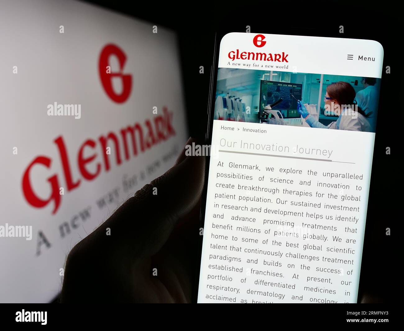 person holding cellphone with webpage of indian company glenmark pharmaceuticals limited on screen with logo focus on center of phone display 2RMFNY3