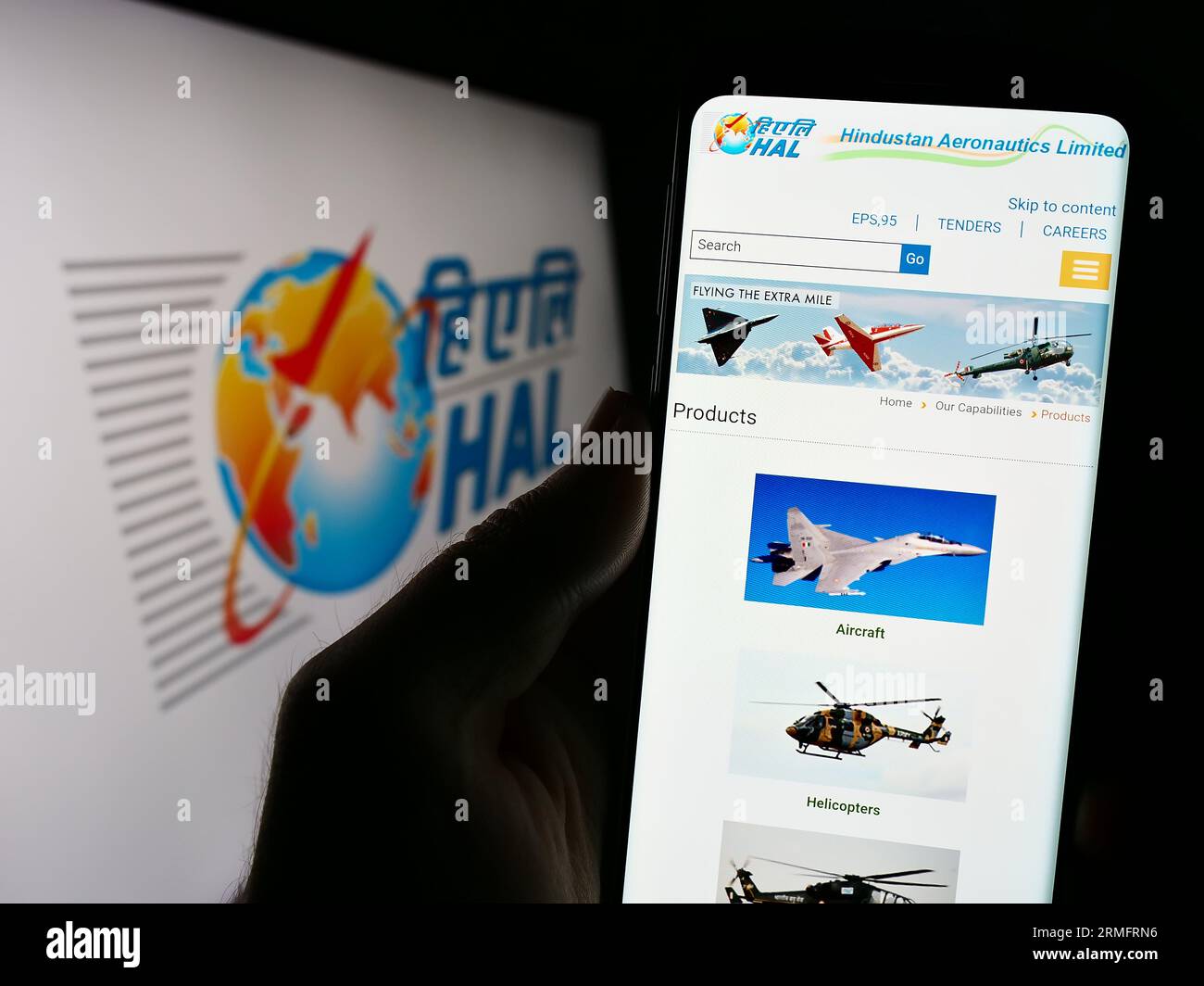 Person holding smartphone with webpage of company Hindustan Aeronautics Limited (HAL) on screen with logo. Focus on center of phone display. Stock Photo