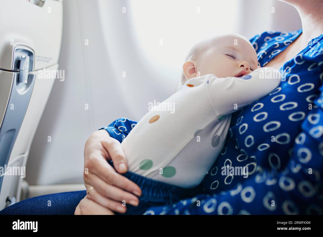 Woman with little girl travelling by plane. Mother holding her sleeping baby during the flight. Travelling with kids Stock Photo