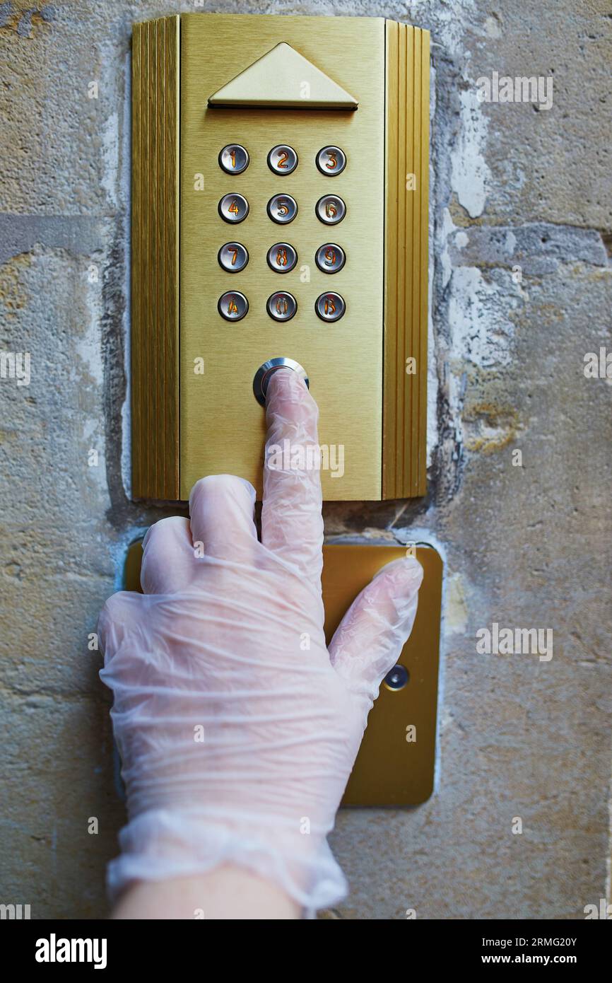 Woman hand in protective single use glove presses house intercome ...