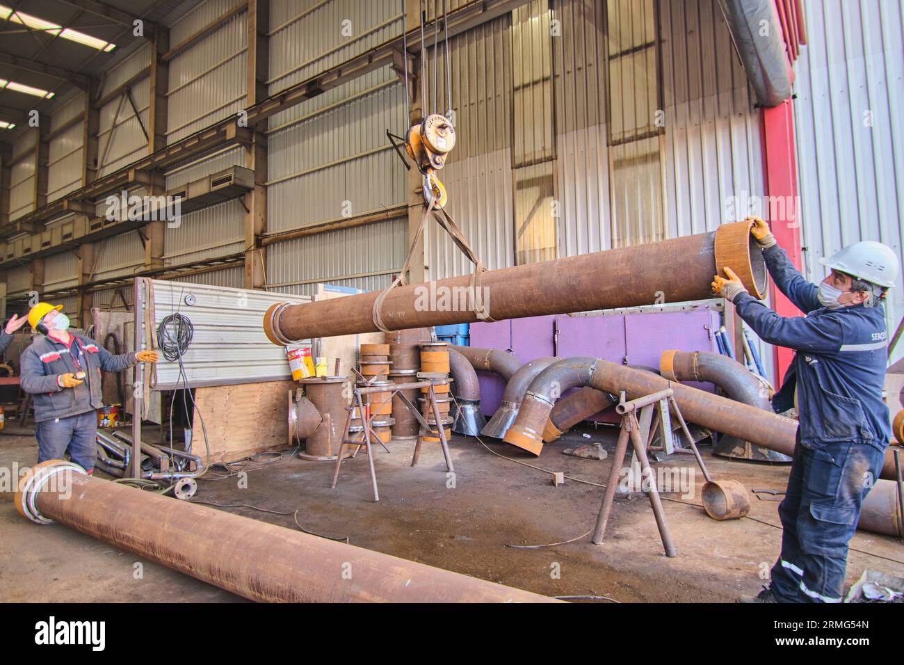 men using a lift and a crane to move big, heavy metal objects like pips ...