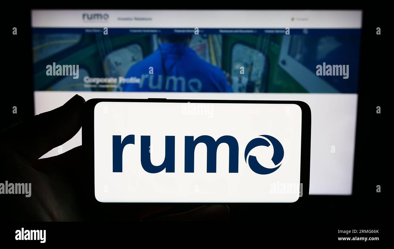 Person holding smartphone with logo of Brazilian logistics company Rumo S.A. on screen in front of website. Focus on phone display. Stock Photo