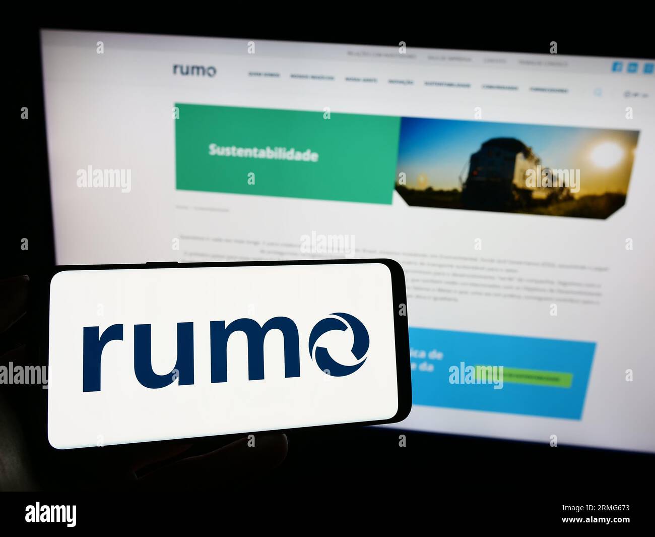 Person holding mobile phone with logo of Brazilian logistics company Rumo SA on screen in front of business web page. Focus on phone display. Stock Photo