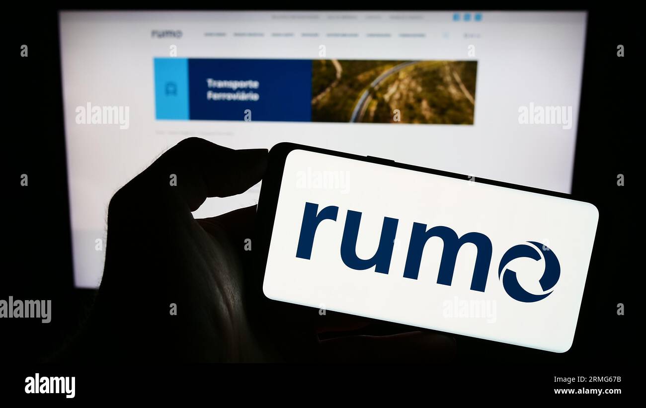 Person holding cellphone with logo of Brazilian logistics company Rumo S.A. on screen in front of business webpage. Focus on phone display. Stock Photo