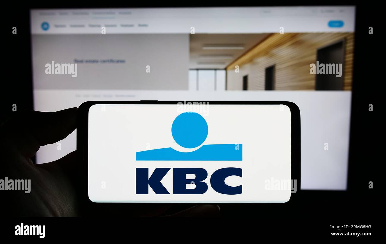 Person holding cellphone with logo of Belgian financial company KBC Group NV on screen in front of business webpage. Focus on phone display. Stock Photo