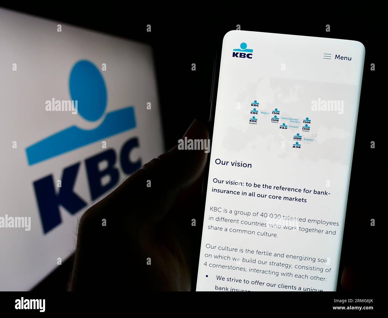 Person holding cellphone with website of Belgian financial company KBC Group N.V.  on screen in front of logo. Focus on center of phone display. Stock Photo