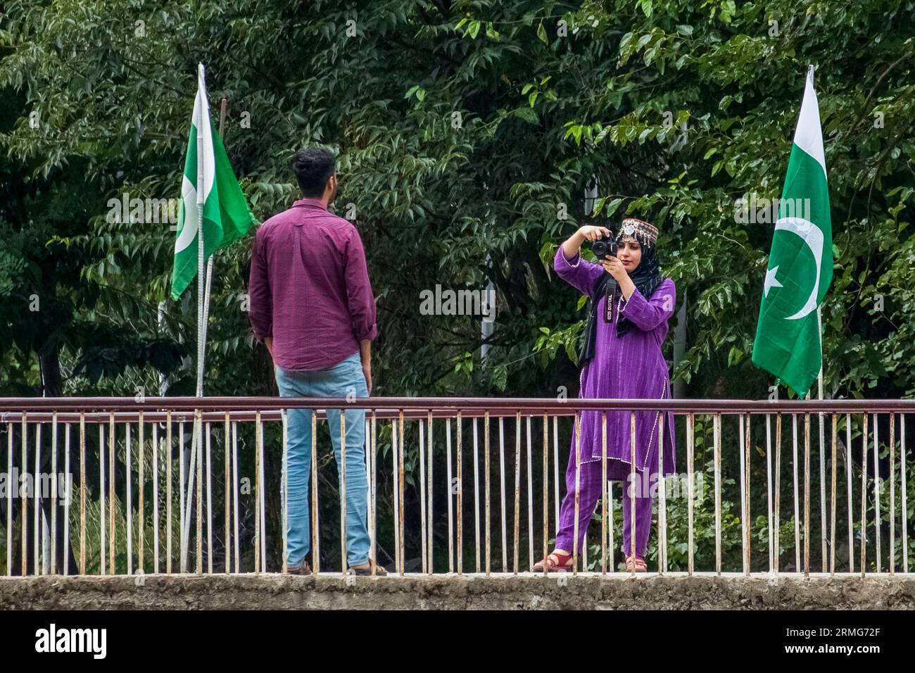 A woman in Pakistan Administered Kashmir seen taking photos of a man in-front of Pakistani flag on the banks of Neelam river or Kishan Ganga that has divided Kashmir into two parts controlled by nuclear rivals India and Pakistan. The river acts as a disputed line of control and flows through a village called Keran from both sides which is located on the northern side of Indian Kashmir's Border district Kupwara some 150kms from Srinagar and 93kms from Muzaffarabad, in the Pakistan side of Kashmir. (Photo by Faisal Bashir/SOPA Images/Sipa USA) Stock Photo