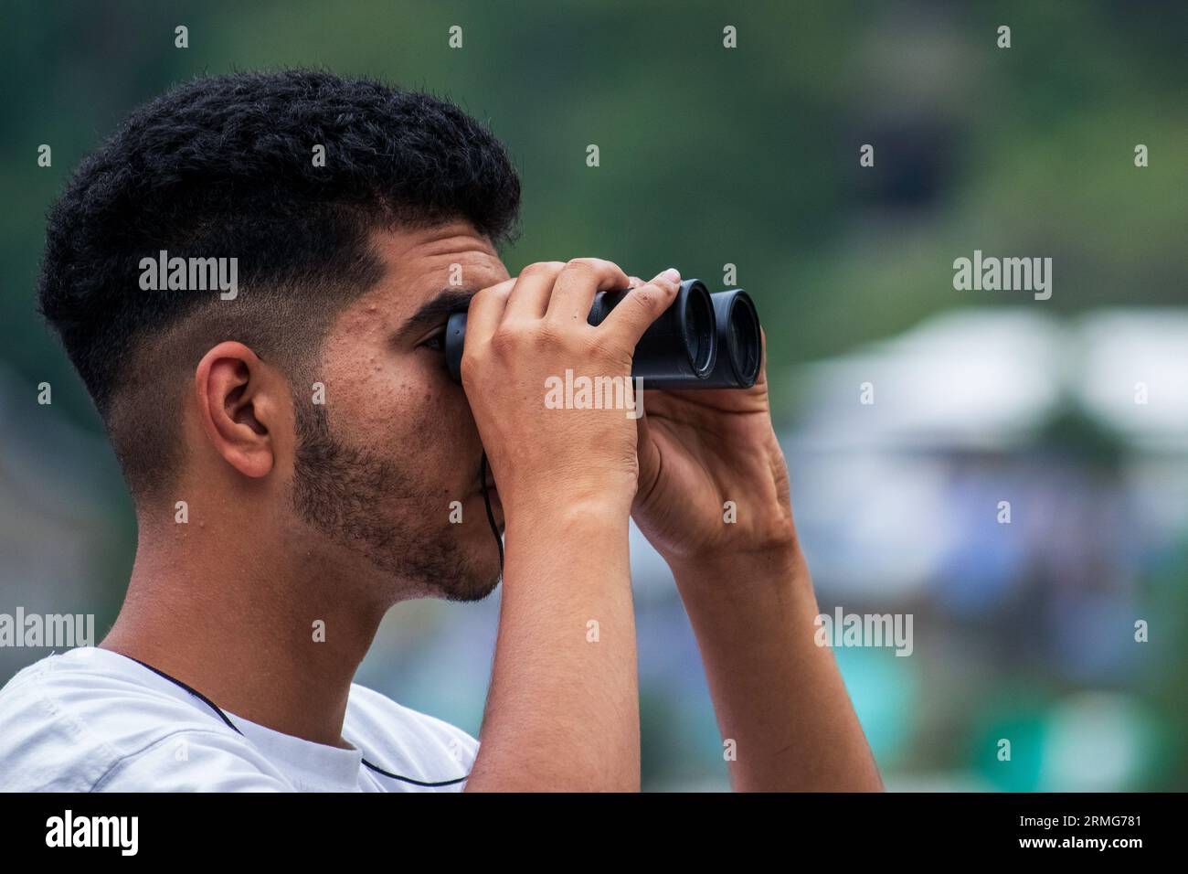 A local visitor in Indian administered Kashmir looks through binoculars towards Pakistan Administered Kashmir on the banks of Neelam river or Kishan Ganga that has divided Kashmir into two parts controlled by nuclear rivals India and Pakistan. The river acts as a disputed line of control and flows through a village called Keran from both sides which is located on the northern side of Indian Kashmir's Border district Kupwara some 150kms from Srinagar and 93kms from Muzaffarabad, in the Pakistan side of Kashmir. (Photo by Faisal Bashir/SOPA Images/Sipa USA) Stock Photo