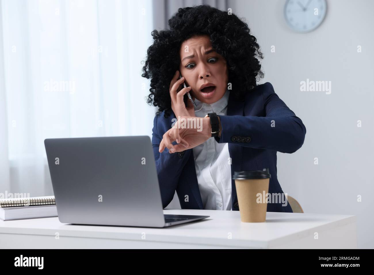 Deadline concept. Scared woman talking on smartphone and checking time in office Stock Photo