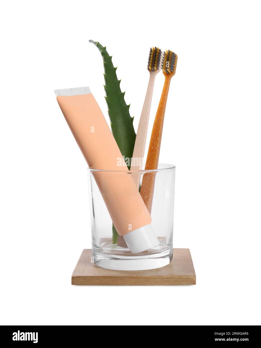 Tube of toothpaste, brushes and aloe vera leaf in glass on white