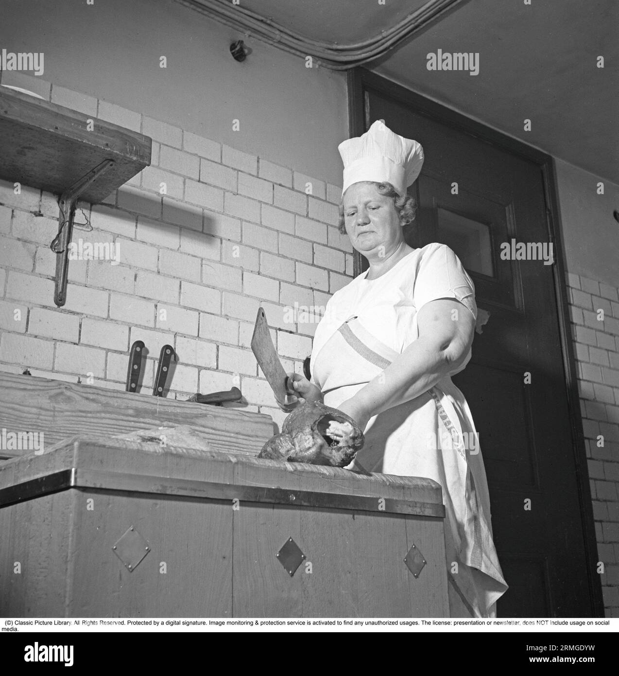 In the kitchen in the 1940s. Interior of a restaurant kitchen and a woman with a large knife, cutting the meat. Sweden 1941. Kristoffersson ref 202-4 Stock Photo