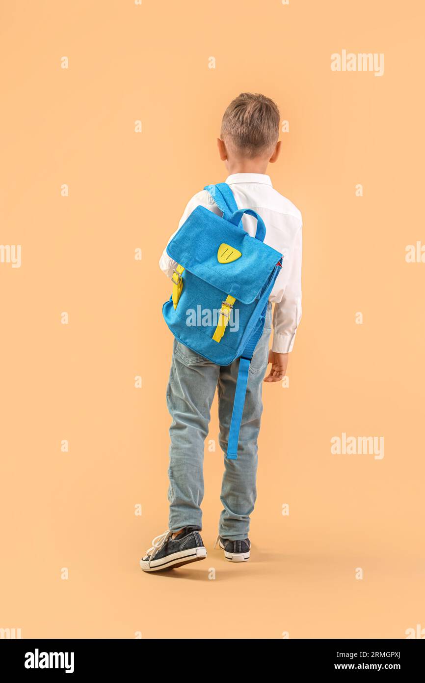 Little schoolboy with blue backpack on orange background, back view ...