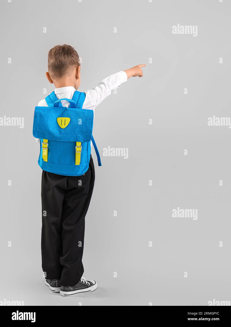 Little schoolboy with blue backpack pointing at something on grey ...