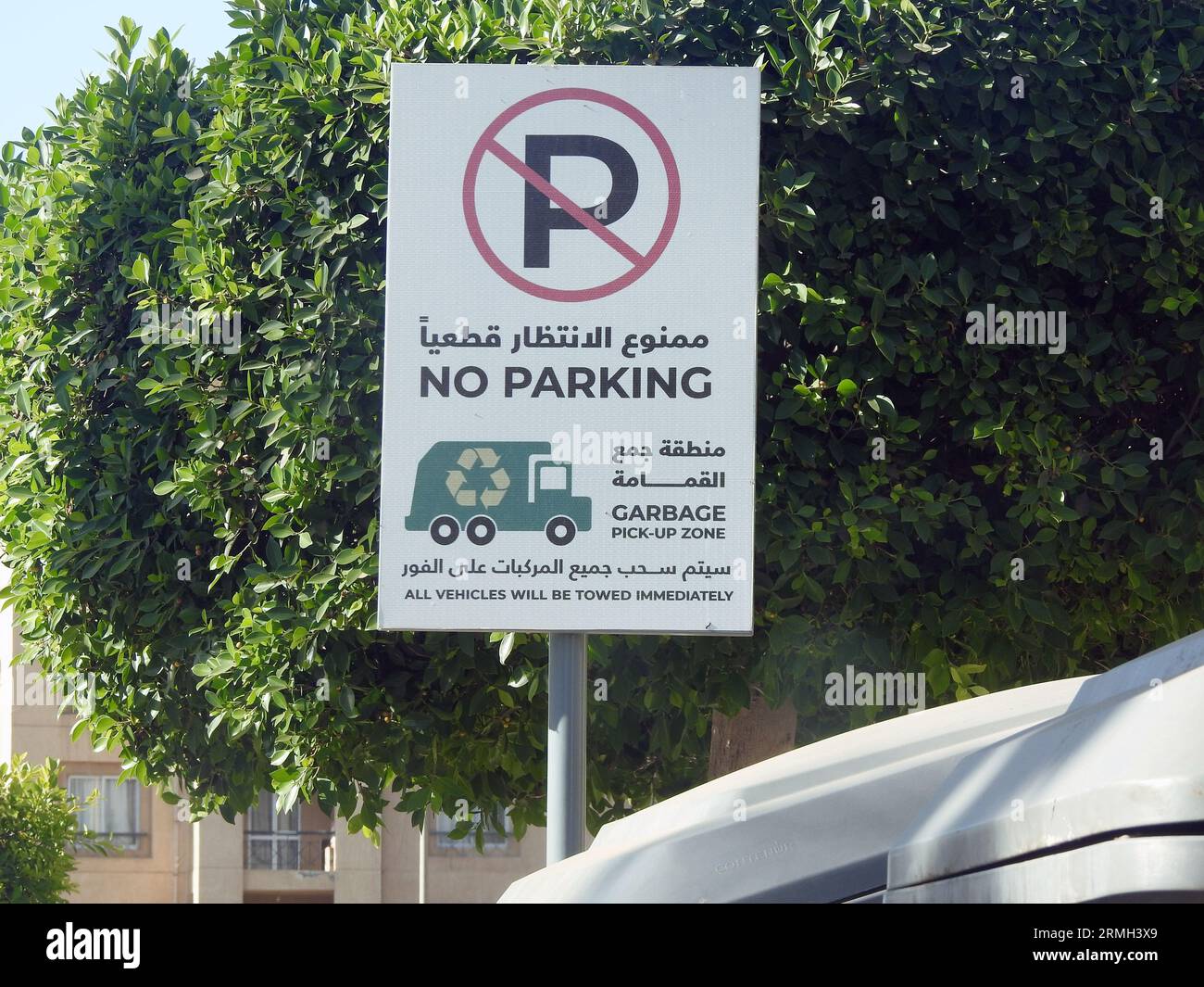 A Road sign in the street near a dumpster litter box in Arabic and