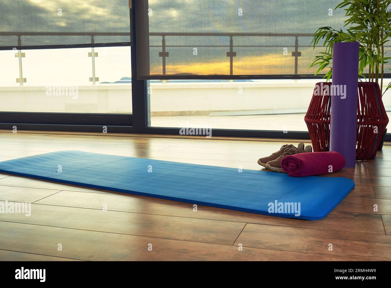 Sunlit fitness room on the top floor of the building with a sunset light. Shoes, mat, roller and belts with towel on the floor ready for raining Stock Photo