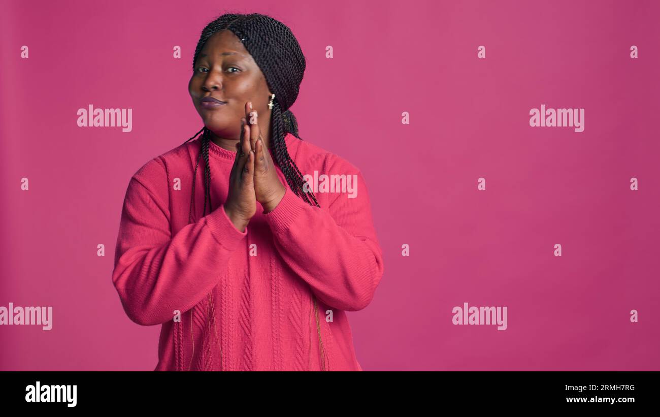Glamorous female with african american ethnicity motioning to the side with left-hand. Stunning black woman with elegant style gesturing and applauding in front of pink color background. Stock Photo
