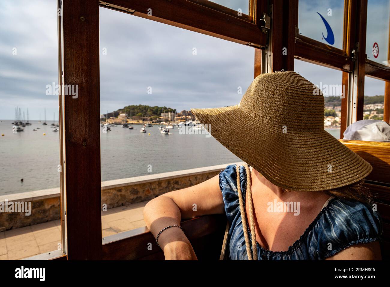 Woman with a summer hat looking through the window of an old train coach at the sea Stock Photo