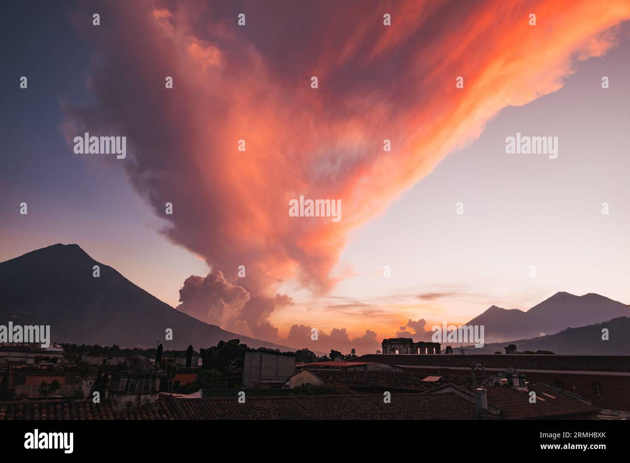A dramatic pink cloud sweeps over the mountains and Spanish colonial rooftops of Antigua, Guatemala, at sunset Stock Photo