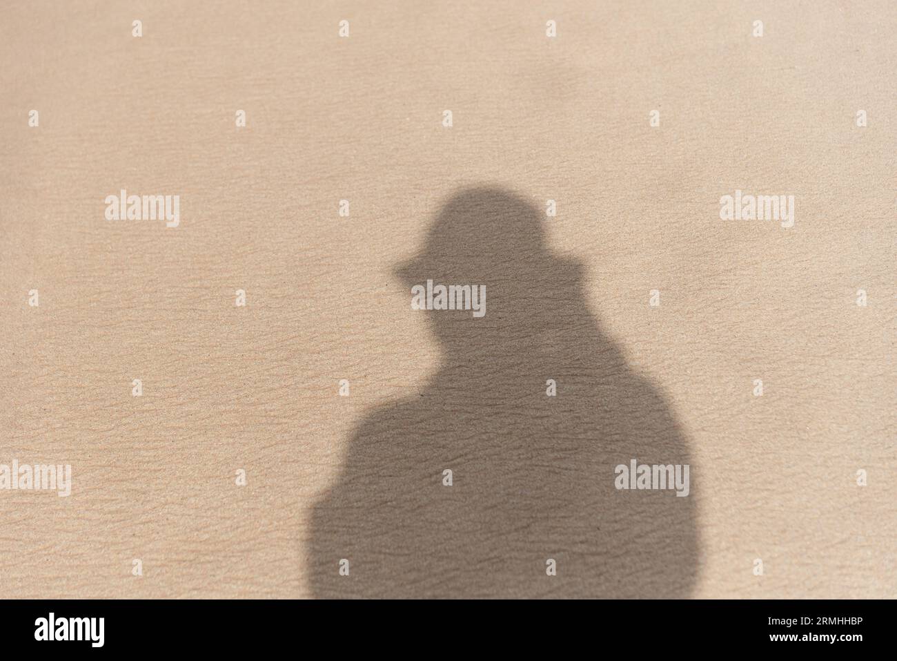 Shadow of a person wearing a hat on the sand of a beach. brown colored sand Stock Photo