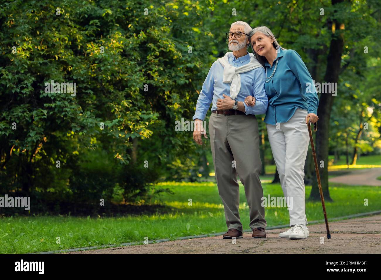 Senior man with walking cane and mature woman in park. Space for text ...