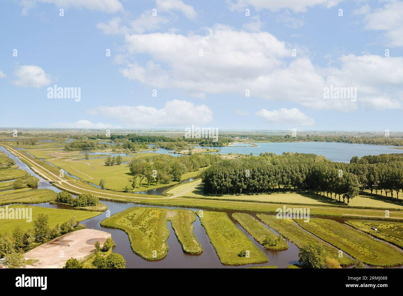 an aerial view of a lake and the land surrounding it is surrounded by trees, grass, and water with clouds in the sky is blue Stock Photo