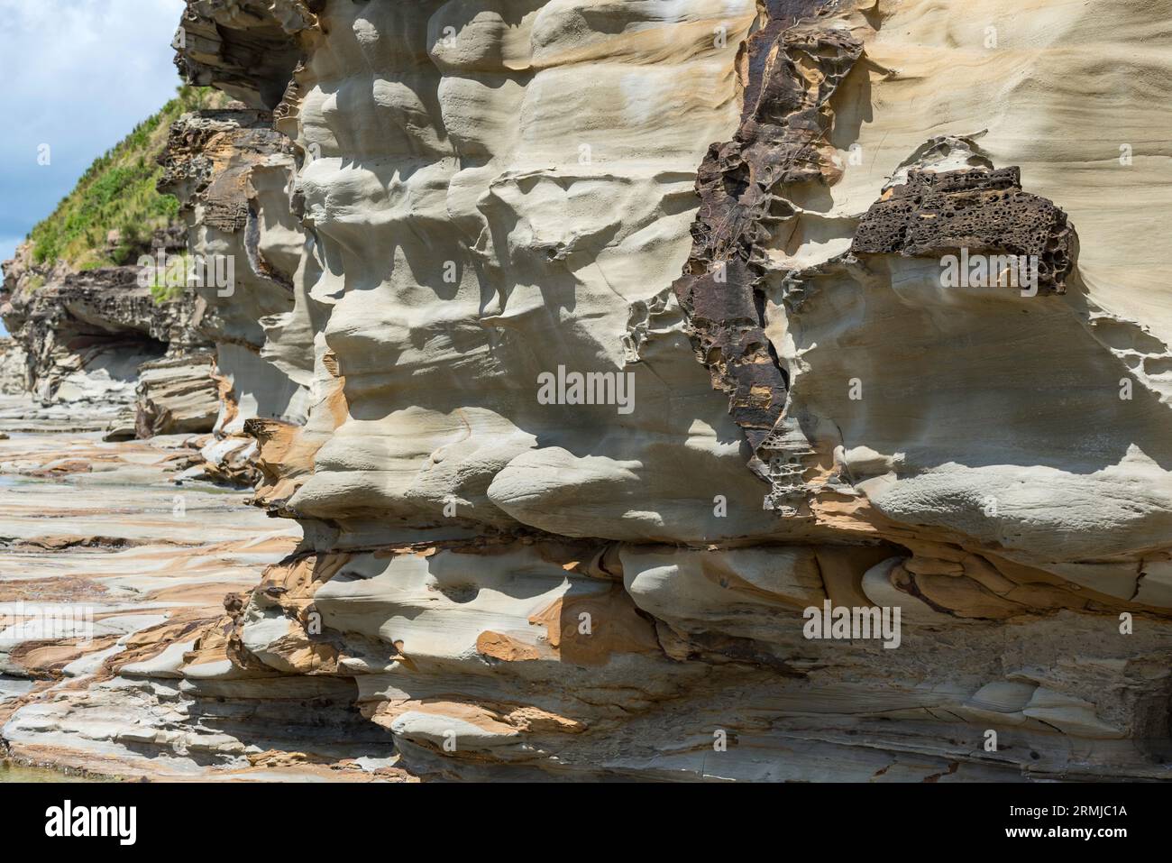 A Hawkesbury Sandstone rock wall and platform at the southern end of Avoca Beach, weathered and worn by constant ocean tides, wind, rain and salt. Stock Photo