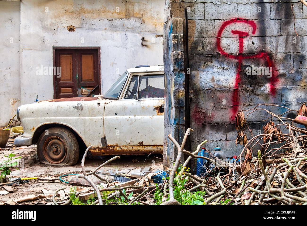 Rusty old car parked next to a brick wall with communism sign (hammer and sickle) on it. The car is a Mercedes-Benz W110, and it is in a state of disr Stock Photo