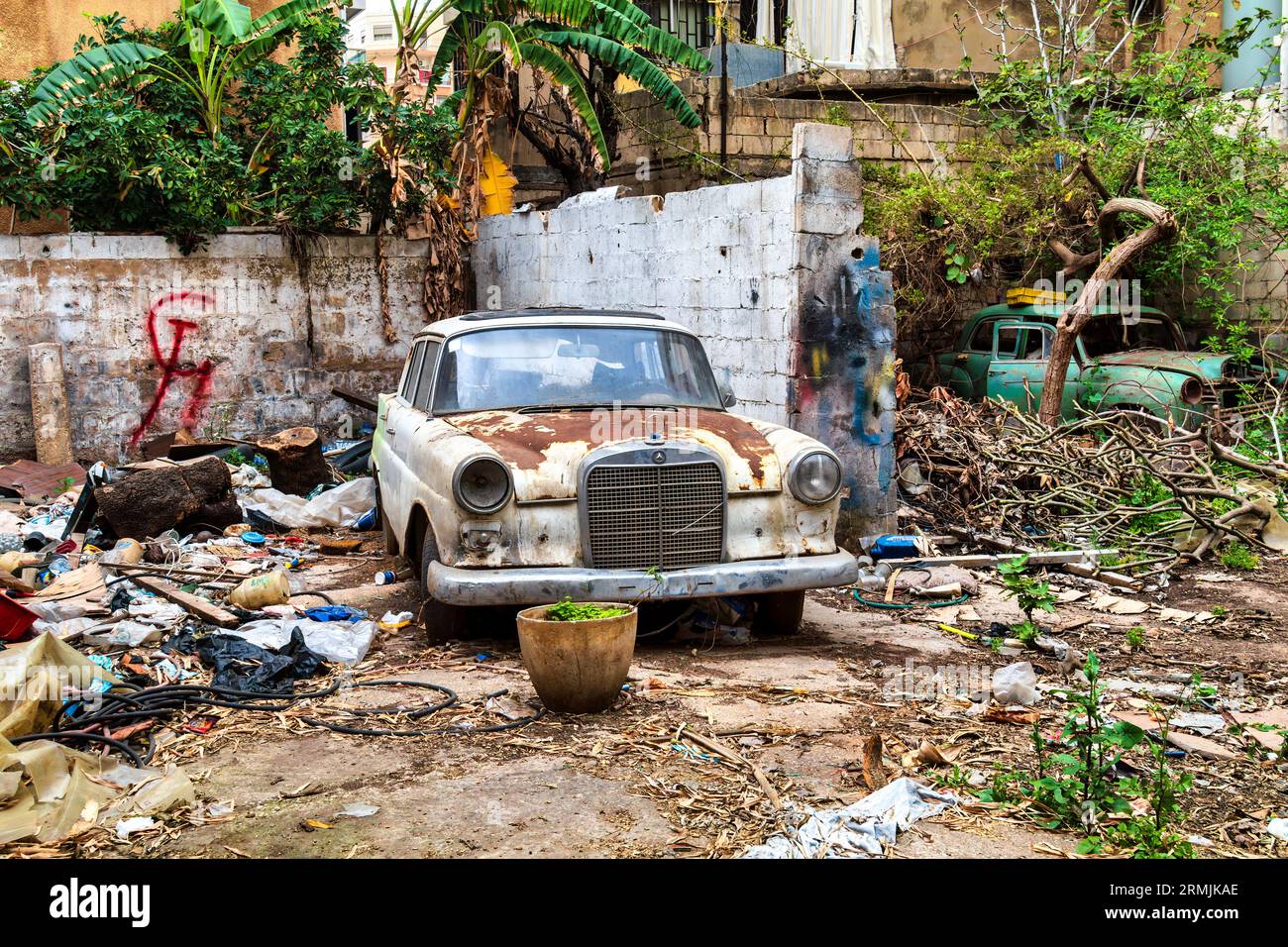 Rusty old car parked next to a brick wall with communism sign (hammer and sickle) on it. The car is a Mercedes-Benz W110, and it is in a state of disr Stock Photo