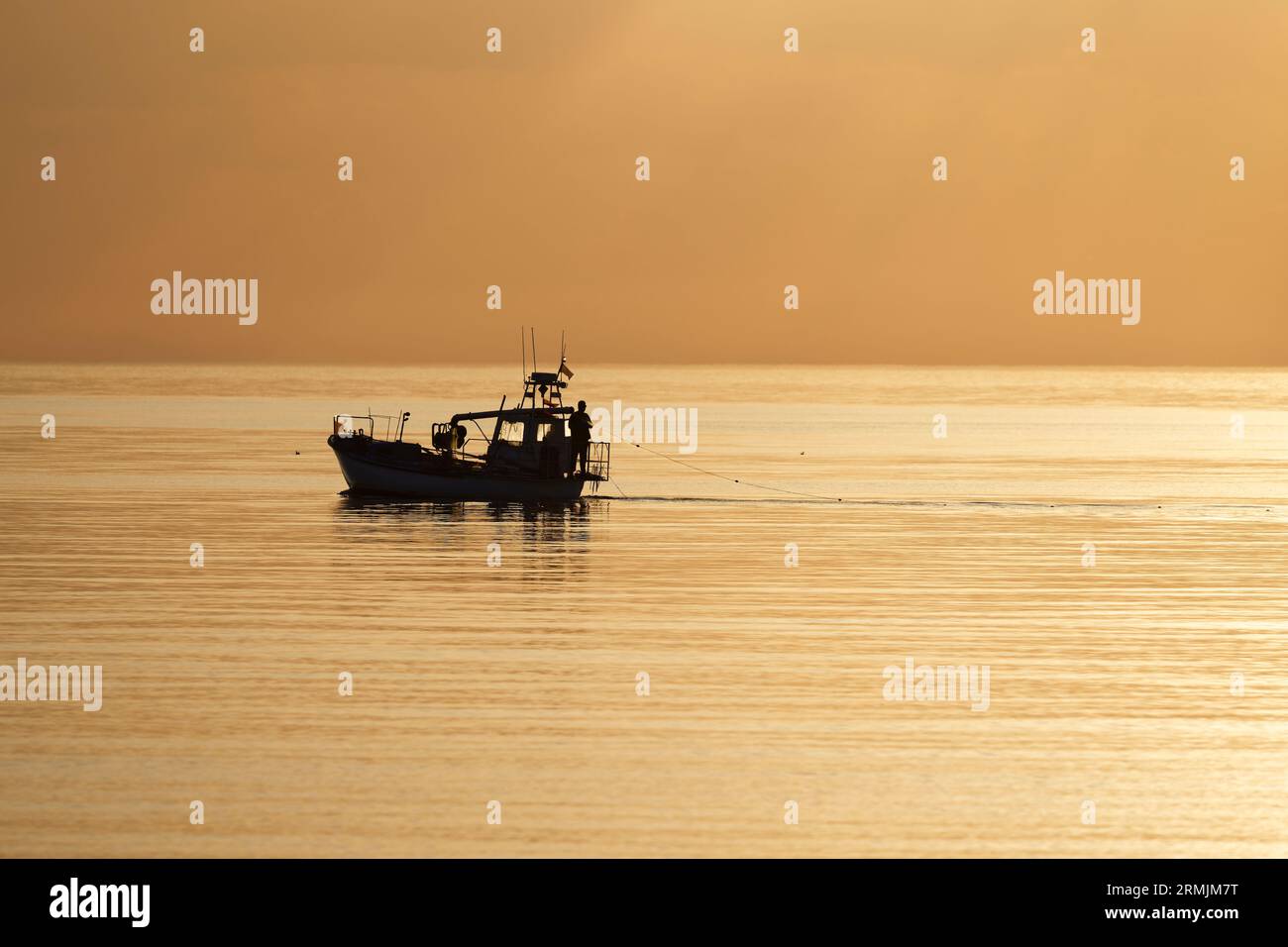 Small commercial fishing boat heading out to calm sea at sunset Stock Photo