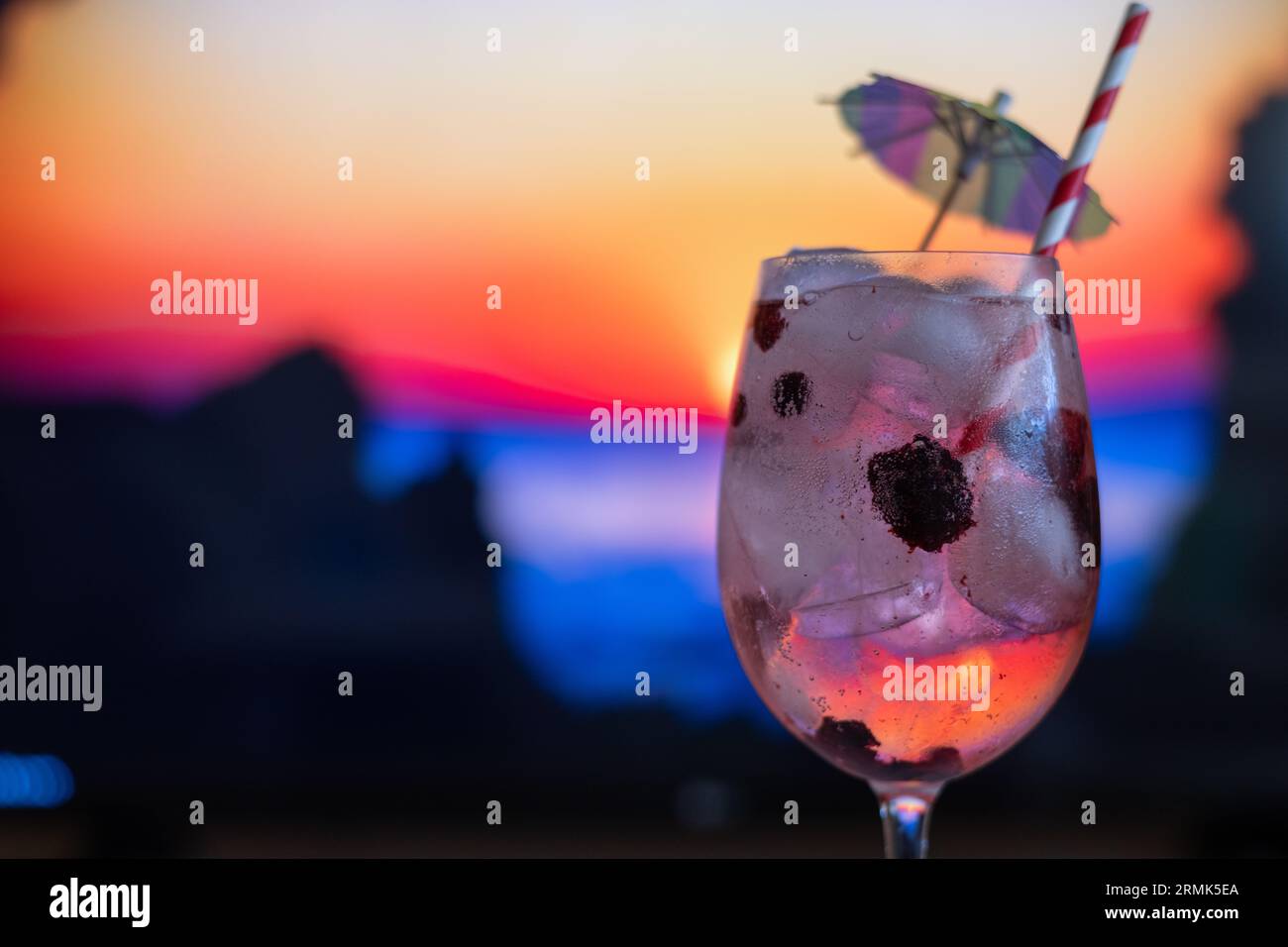 Cocktail On The Counter Of A Beach Bar At Sunset. Alcoholic Drink With berries Fruits, With Straw And Umbrella Stock Photo