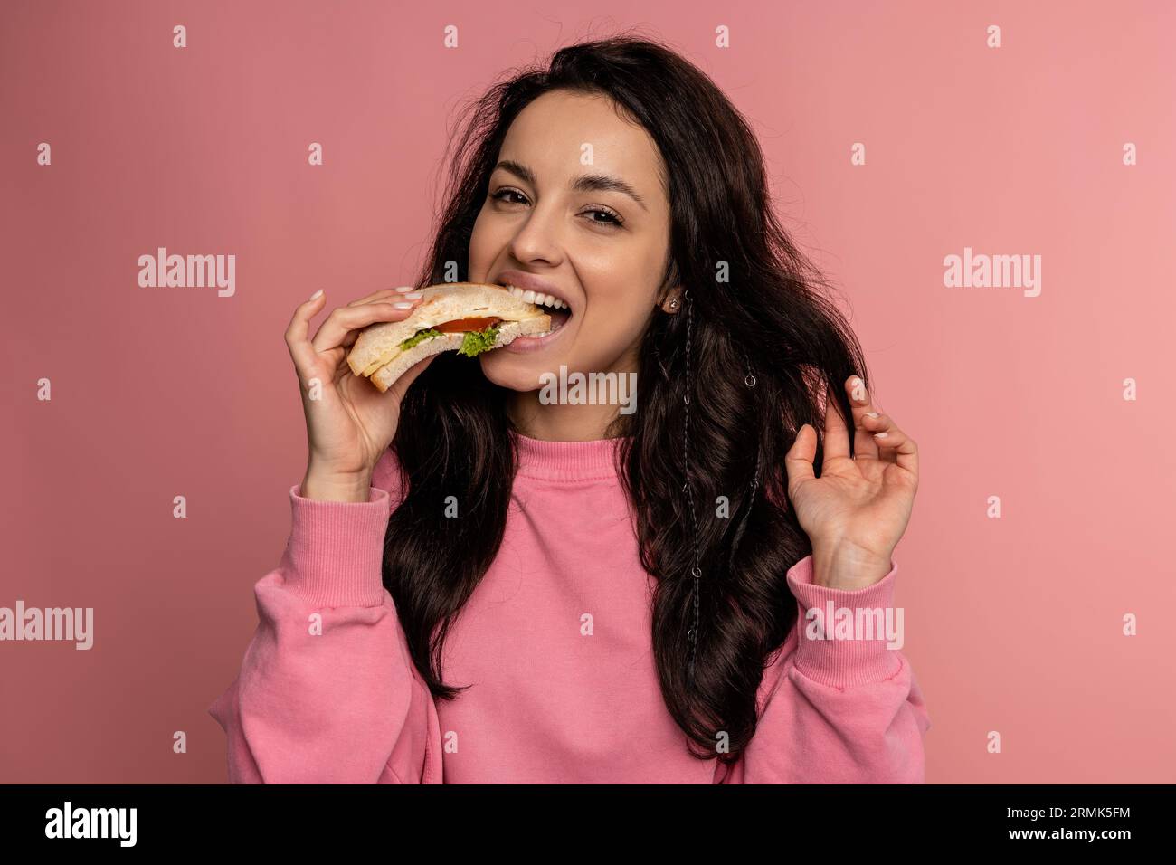 Hungry young dark-haired lady dressed in the jumper enjoying her nutritious sarnie in front of the camera. Healthy snack concept Stock Photo