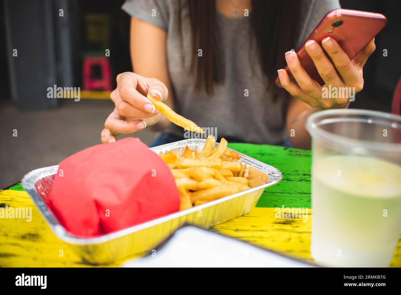 Close up girl with phone eating fries Stock Photo