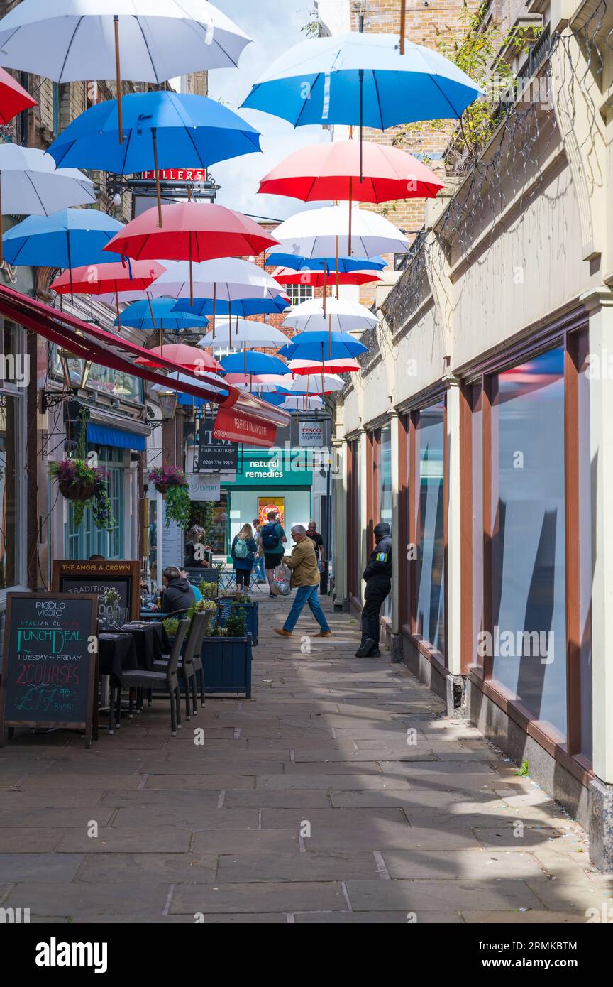 View along Church Court hung overhead with colourful umbrellas, a narrow alley of shops and a pub. Richmond, London, England, UK Stock Photo